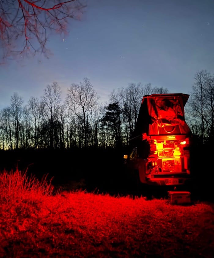 image of a camper parked in a field at night with red night lights lit up