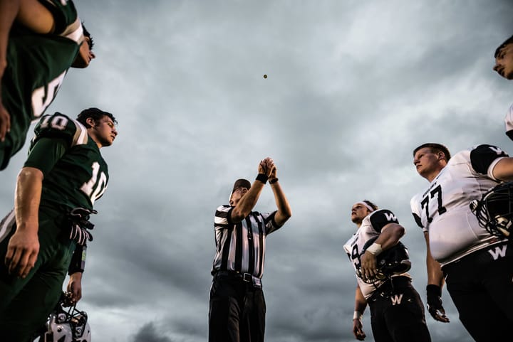 Image of a football referee flipping a coin with one team standing to the referee's left and the other to his right.