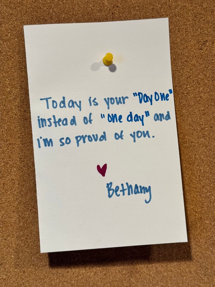 Picture of a hand-written note stuck to a cork board that reads "Today is your "day one" instead of "one day" and I'm so proud of you. [heart] Bethany